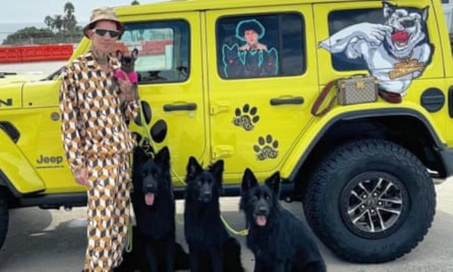 Augusto Deoliveira standing with three dogs by a yellow Humvee-style vehicle with dog branding and stickers on them