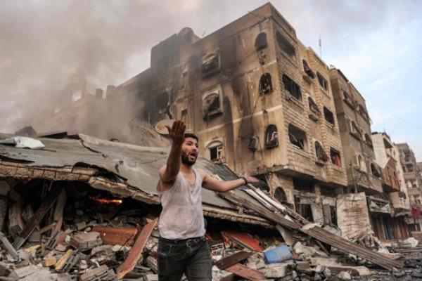 TOPSHOT - A man reacts outside a burning collapsed building following Israeli bombardment in Gaza City on October 11, 2023. At least 30 people have been killed and hundreds wounded as Israel pounded the Gaza Strip with hundreds of air strikes overnight, a Hamas government official said on October 11. The Israeli military co<em></em>nfirmed it had hit several Hamas targets during the night in the Palestinian enclave. (Photo by MOHAMMED ABED / AFP) (Photo by MOHAMMED ABED/AFP via Getty Images)