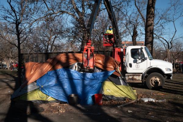 A tent getting dismantled by city workers.