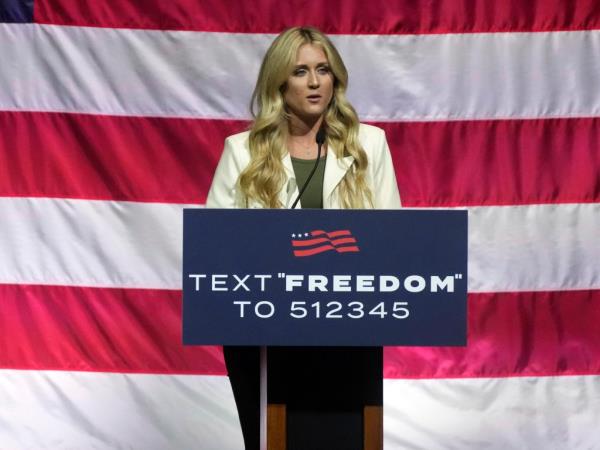 Riley Gaines speaks at a podium in front of an American flag. 