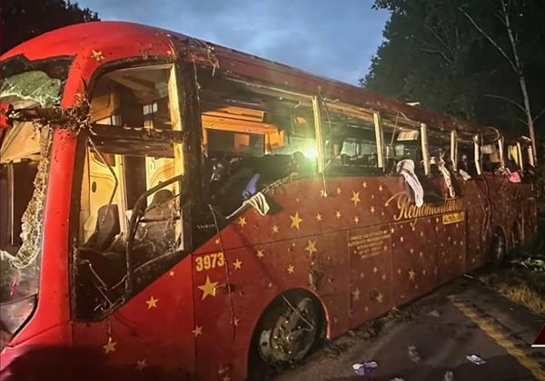 The battered red charter bus, with almost all of the windows broken and clothing hanging out of several of them. 