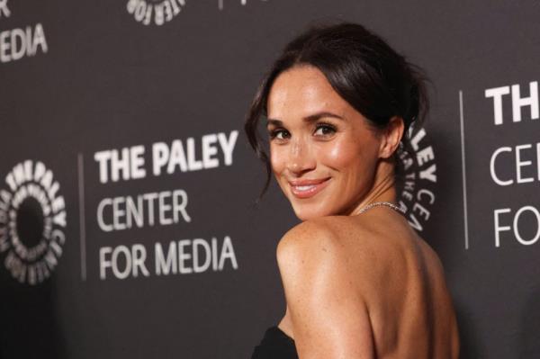 Meghan, Duchess of Sussex, smiling at the camera while attending the Paley Ho<em></em>nors Gala in Beverly Hills, wearing a custom Logan Hollowell necklace and a Cartier Love bracelet