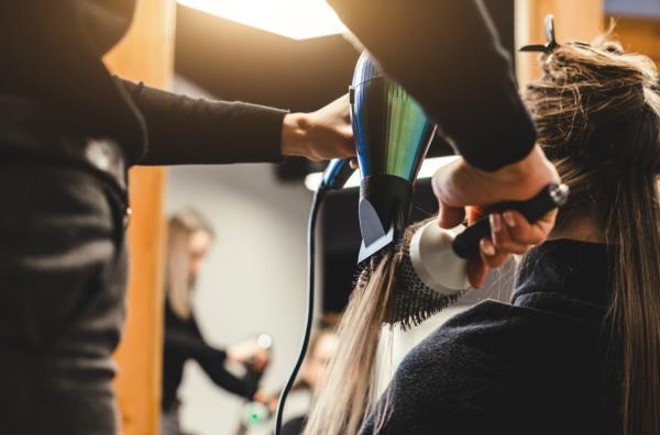 Master woman hairdresser dries the girl's hair with a hairdryer after washing in a beauty salon, close up.