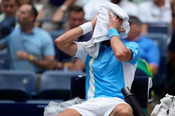 Novak Djokovic tries wipe sweat with a towel.