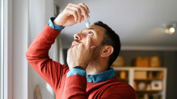 A man in a red sweater puts in eye drops.