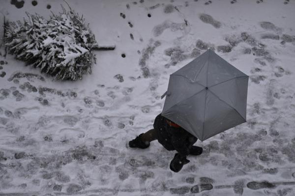 A person seen from above carrying an umbrella walks along a snowy sidewalk in Brooklyn.