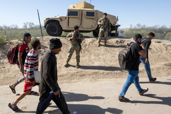 Immigrants from Venezuela walking in front of a military vehicle in Eagle Pass, Texas.