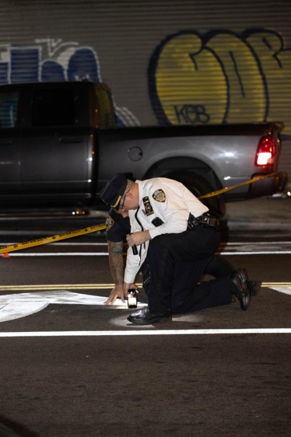 Two police officers look at the street at a shooting scene.