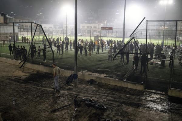 Residents and authorities stand at a soccer field that was hit by a rocket.