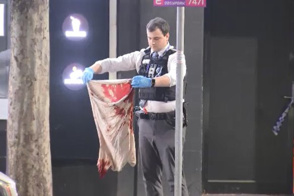 An officer holding a bloodstained shirt after the alleged stabbing spree.